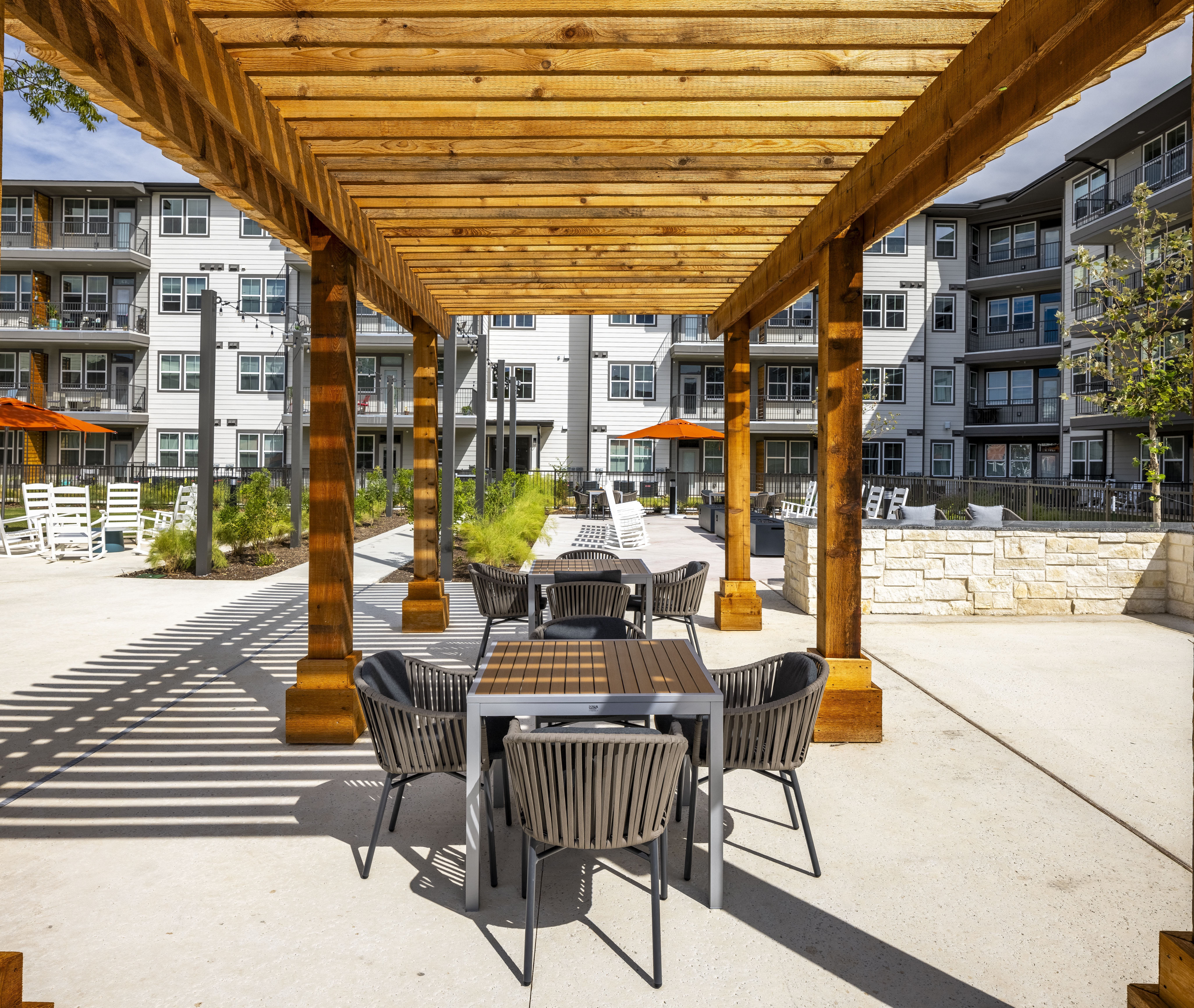 a patio with tables and chairs under a wooden pergola at a senior apartment community
